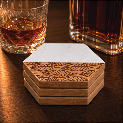 Set of four faux marble and acacia wood hexagon coasters featuring an engraved falling leaves pattern, styled beside a whiskey glass and decanter.