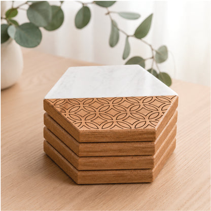 Set of four hexagon marble and acacia wood coasters stacked neatly on a light wood tabletop, featuring a geometric engraved pattern on the wood portion and a white marble upper section, styled in a bright modern home setting with soft greenery in the background.