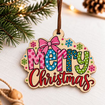 A wooden Christmas ornament with a scalloped edge and a hanging loop, featuring the words “Merry Christmas” in colorful patterned letters with a pink bow and snowflake accents. The ornament is styled on a white fabric surface with pine branches and warm string lights in the background.