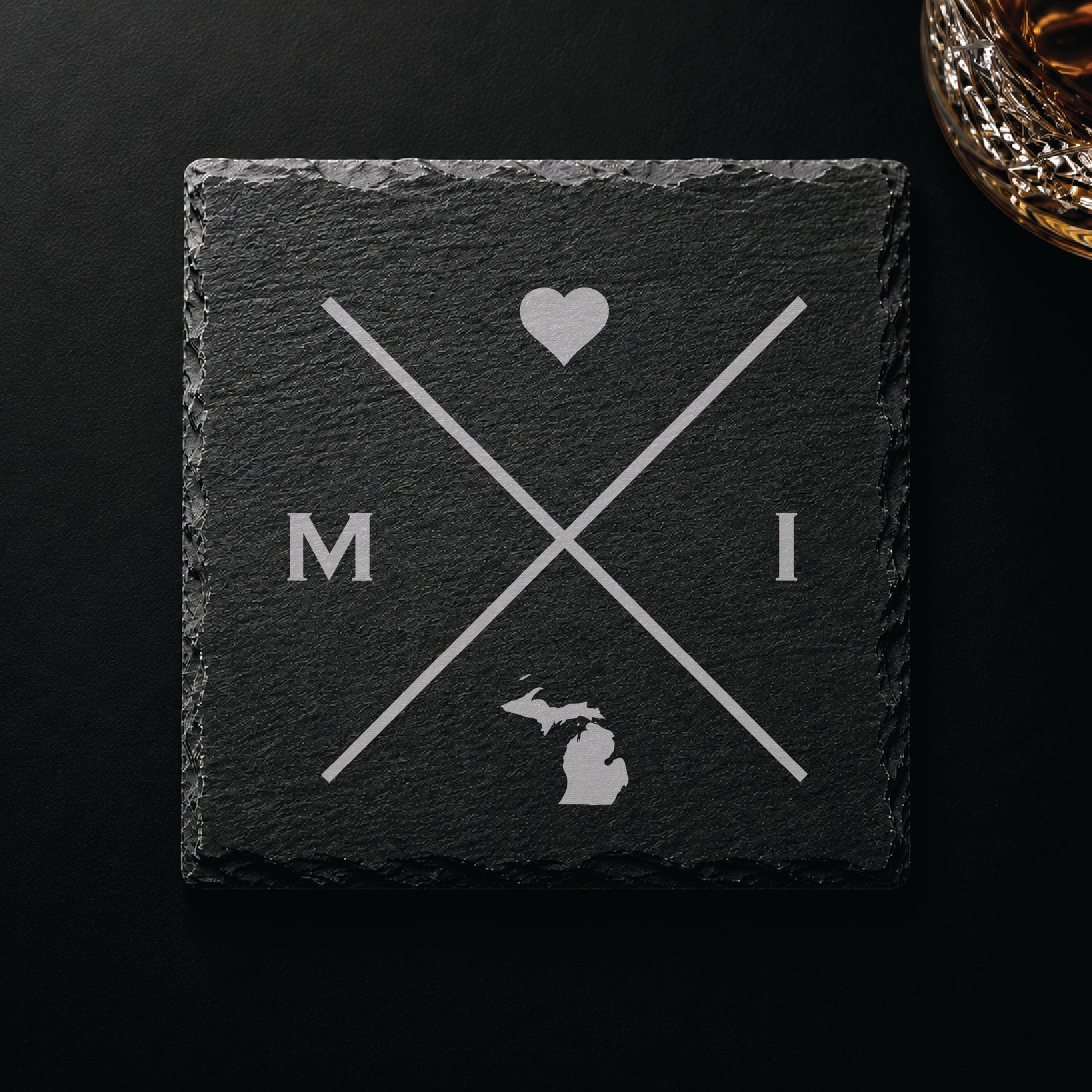 Dark slate coaster with engraved Michigan crossed-line design, heart icon, and Michigan silhouette on a dark background.