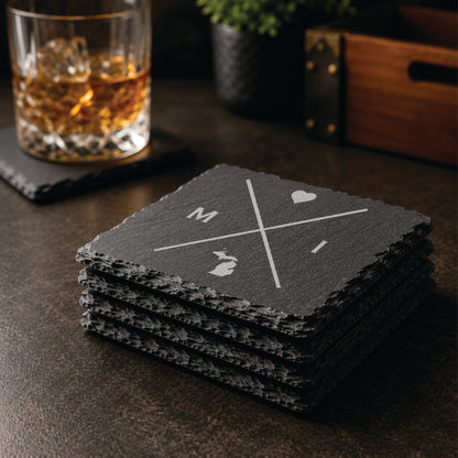 Stack of engraved Michigan slate coasters in a warm bar-style setting with whiskey glass nearby, featuring a minimalist crossed-line Michigan design.