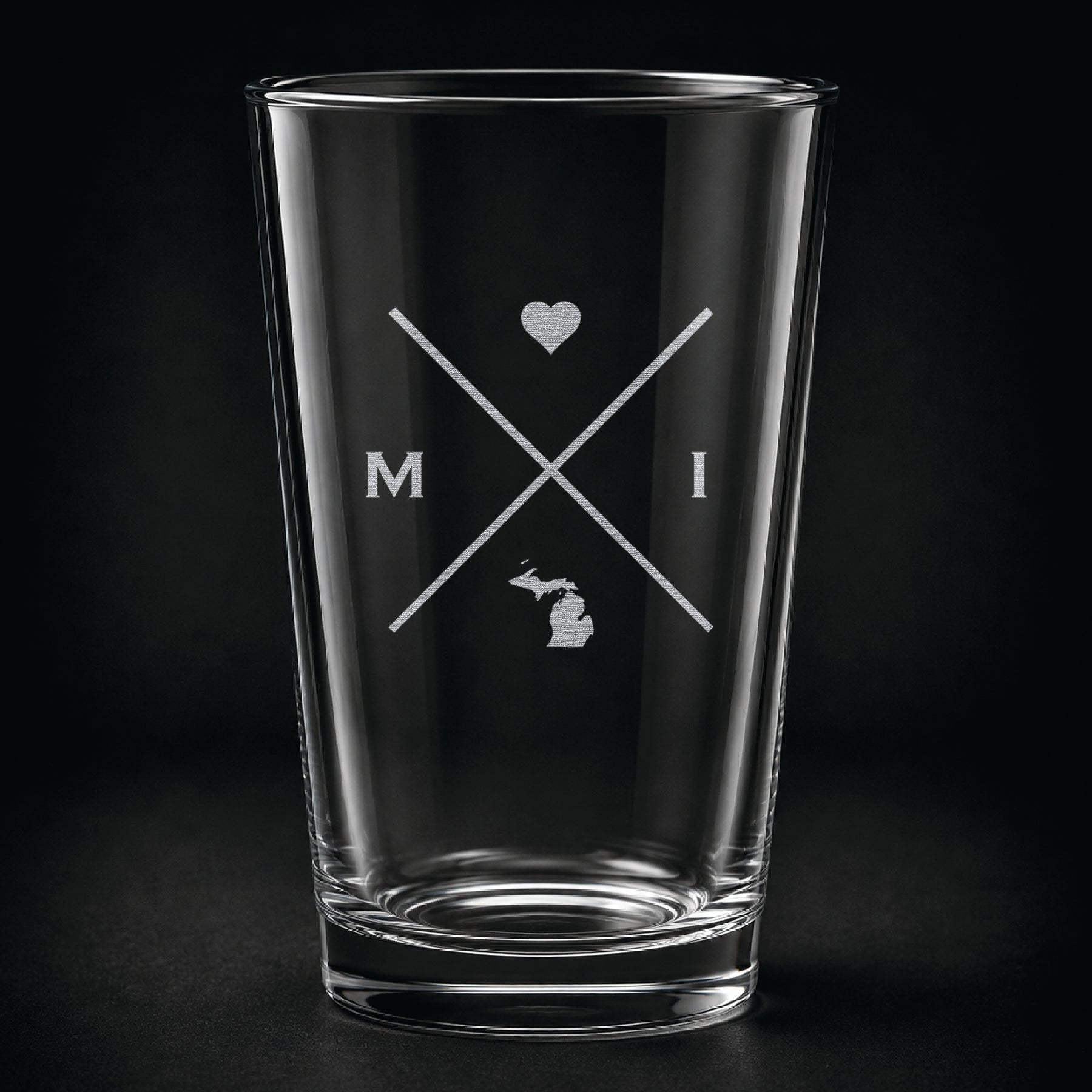 Engraved Michigan pint glass featuring a minimalist crossed-line design with heart detail and Michigan silhouette on a dark background.