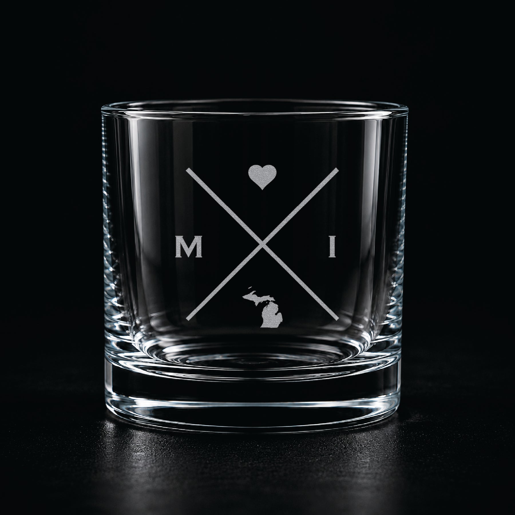 Engraved Michigan rocks glass with frosted Michigan silhouette and crossed-letter monogram on a dark background.
