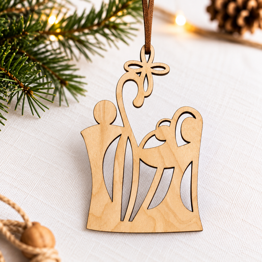 A natural wood hanging ornament shaped like a stylized nativity scene with a star at the top, displayed on a white textured surface with pine branches and warm string lights in the background.
