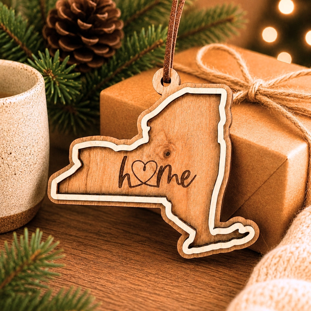 Layered New York wood ornament with engraved “home” script displayed beside wrapped holiday gifts, greenery, and warm seasonal décor.