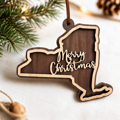 Layered hardwood New York Christmas ornament featuring walnut and maple wood with “Merry Christmas” script detail and faux leather hanger styled with evergreen branches and warm holiday lights.