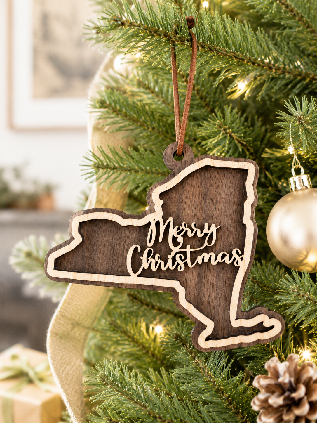 Layered New York state Christmas ornament hanging on a decorated holiday tree, featuring walnut and maple wood tones, “Merry Christmas” script, warm white lights, and neutral festive décor.