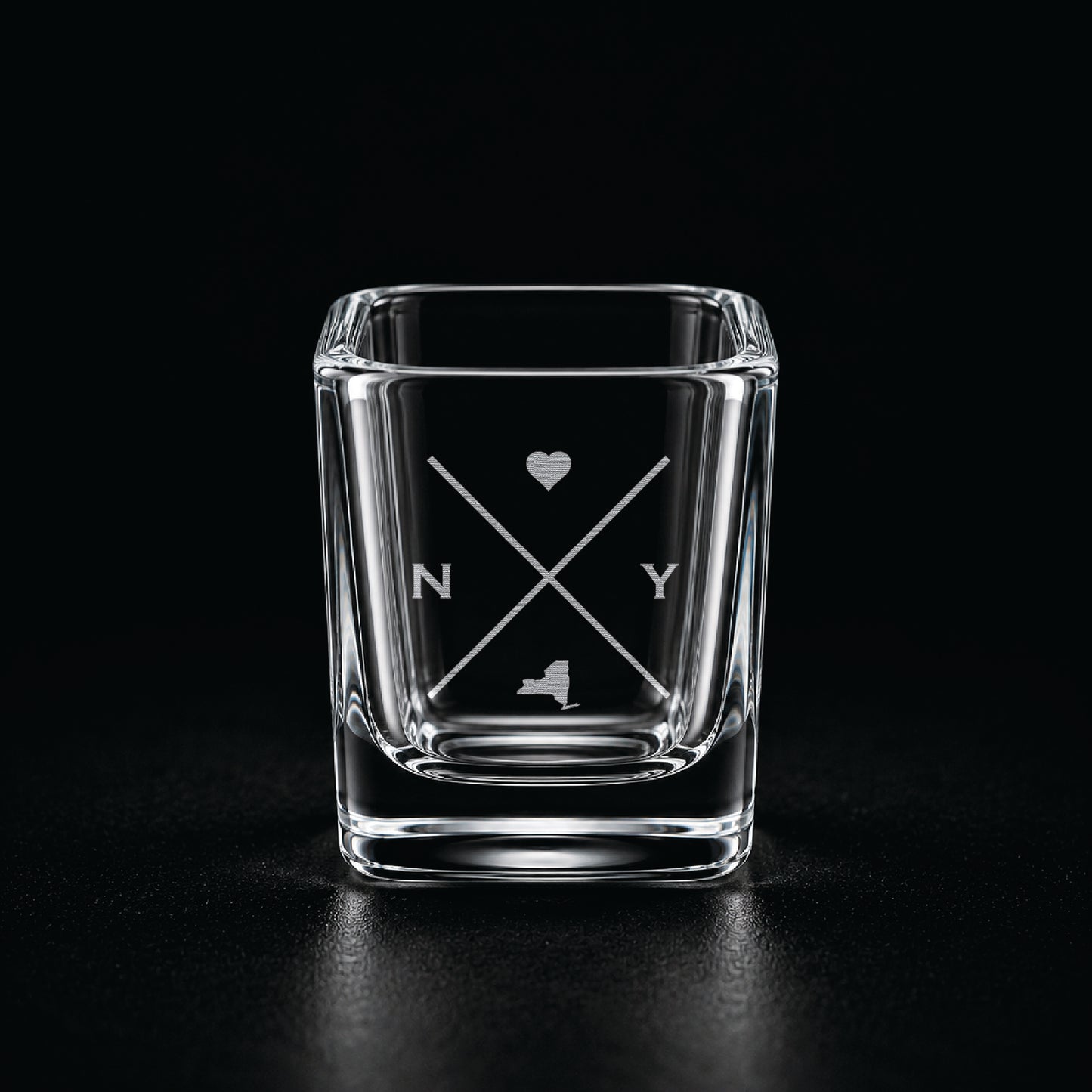 Engraved New York shot glass with modern crossed-line state design and frosted laser engraving on a dark background.