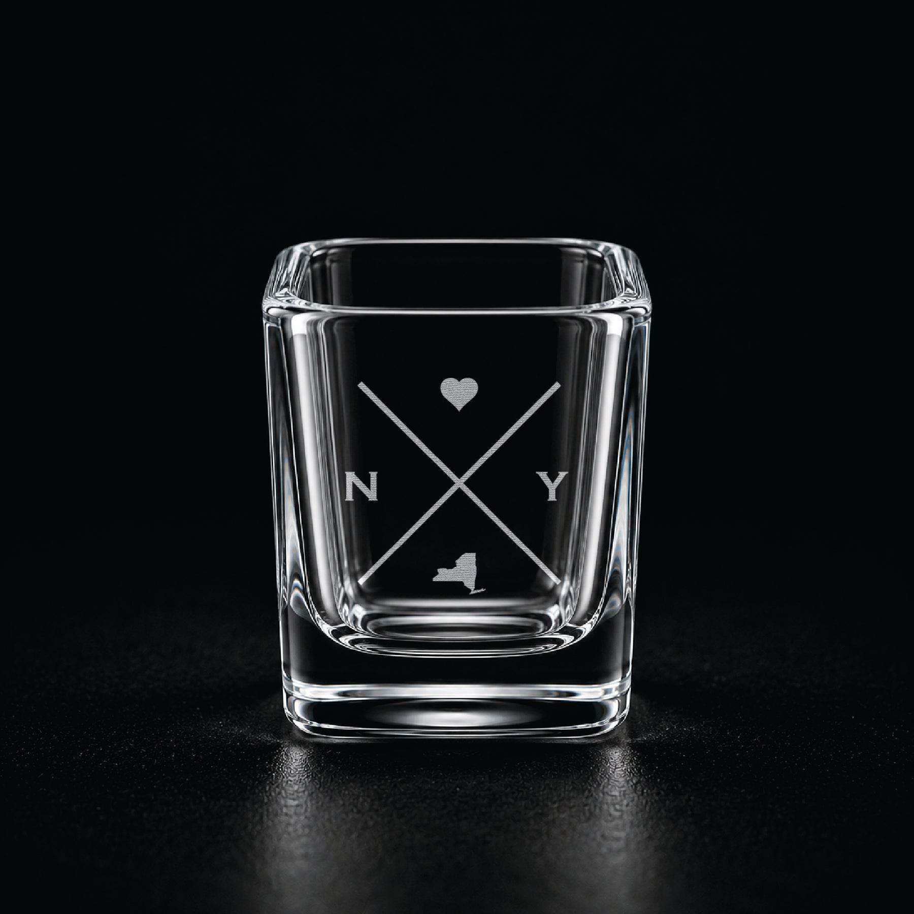 Engraved New York shot glass with modern crossed-line state design and frosted laser engraving on a dark background.