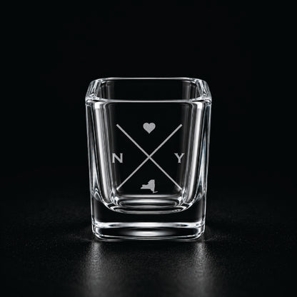 Engraved New York shot glass with modern crossed-line state design and frosted laser engraving on a dark background.