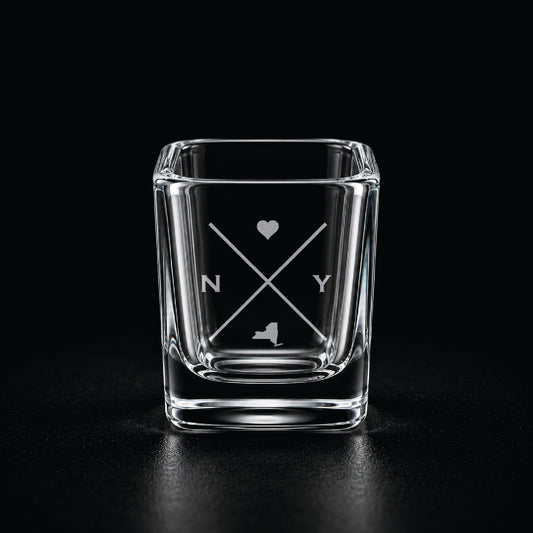 Engraved New York shot glass with modern crossed-line state design and frosted laser engraving on a dark background.