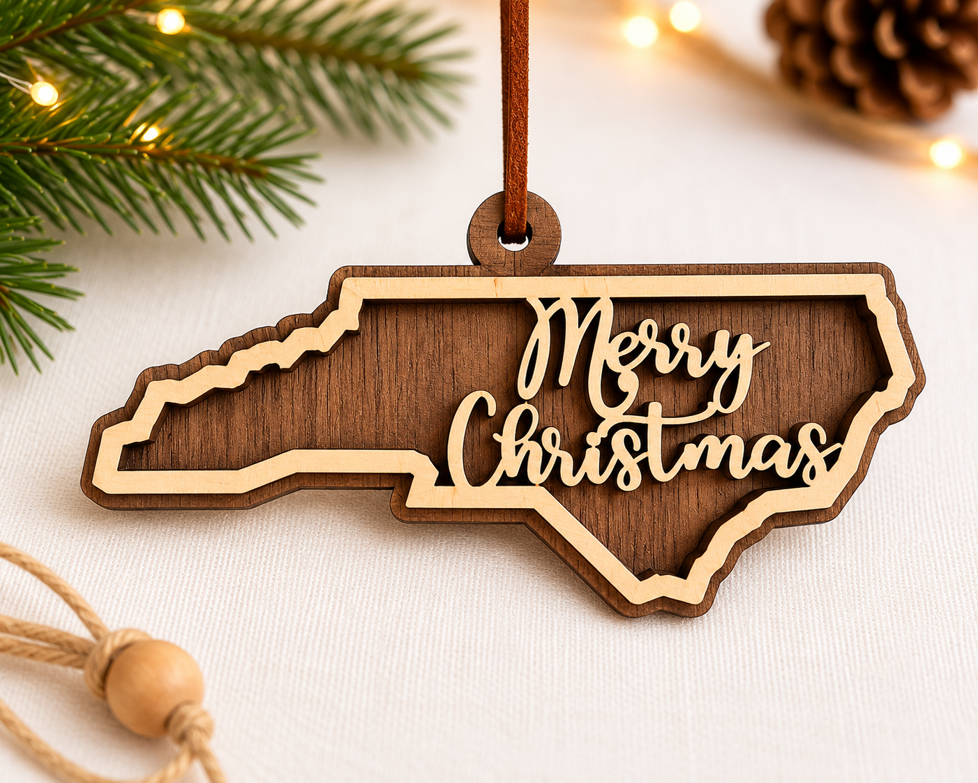 Wooden Christmas ornament shaped like North Carolina with 'Merry Christmas' text, surrounded by festive decorations.