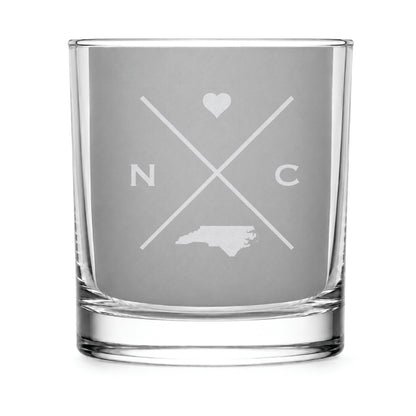 Clear engraved rocks glass featuring a minimalist crossed-line North Carolina  design with monogram initials, heart icon, and North Carolina silhouette on a clean light background.