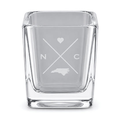 Clear engraved North Carolina shot glass featuring a minimalist crossed-line design with heart detail and North Carolina silhouette on a clean light background.