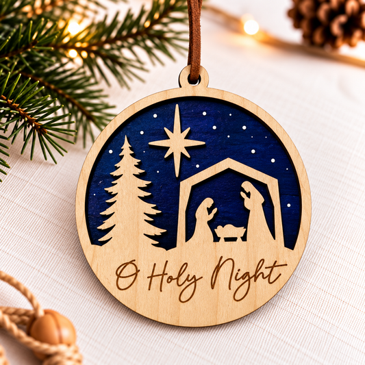 A round wooden Christmas ornament with a laser-cut nativity scene and the engraved text 'O Holy Night' on a light wood surface, hanging against a softly lit holiday background with pine branches and warm lights.