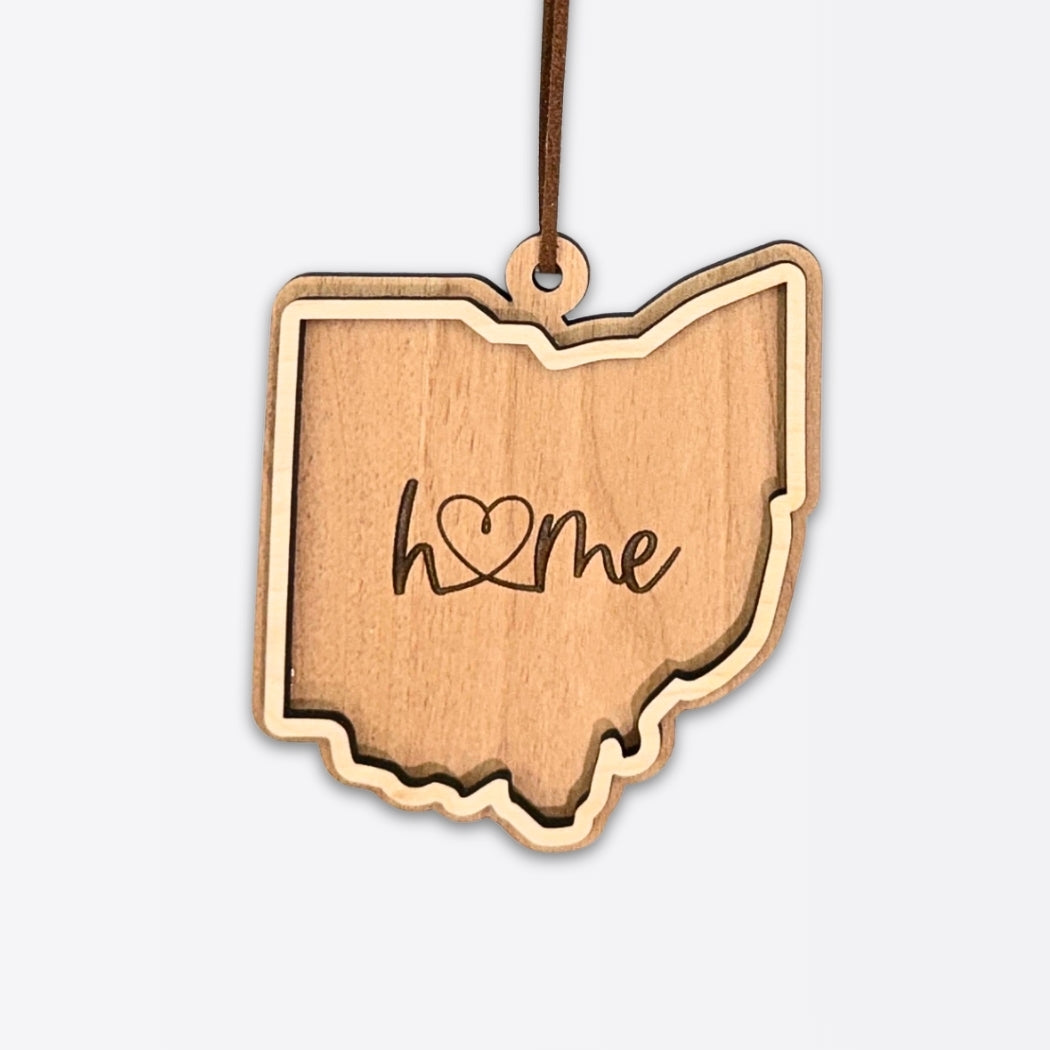 Layered Ohio wood ornament with engraved “home” script and faux leather cord on white background.