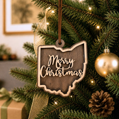 Wooden 'Merry Christmas' ornament shaped like the state of Ohio hanging on a decorated Christmas tree.