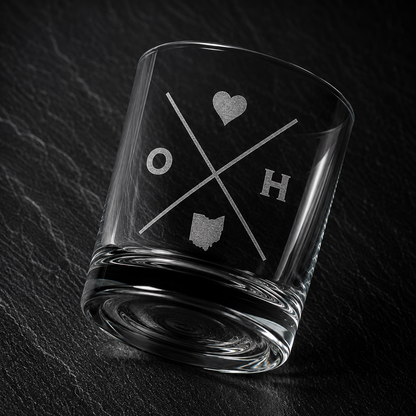 Angled engraved Ohio whiskey glass featuring frosted Ohio silhouette and modern crossed-letter design on a dark textured surface.