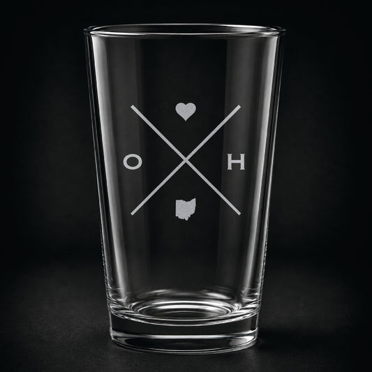 Engraved Ohio pint glass featuring a minimalist crossed-line design with heart detail and Ohio silhouette on a dark background.