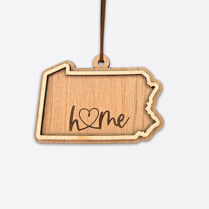 Layered Pennsylvania wood ornament with engraved “home” script and faux leather cord on white background.
