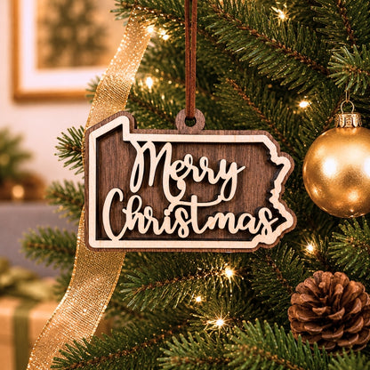 Layered Pennsylvania state Christmas ornament hanging on a decorated holiday tree, featuring walnut and maple wood tones, “Merry Christmas” script, warm white lights, and neutral festive décor.