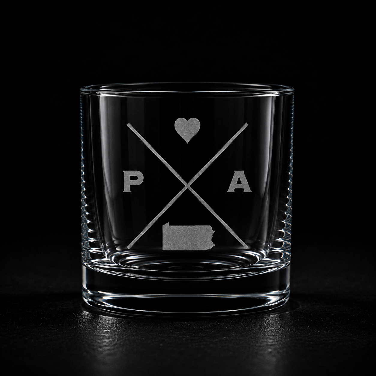 Engraved Pennsylvania rocks glass with frosted Pennsylvania silhouette and crossed-letter monogram on a dark background.