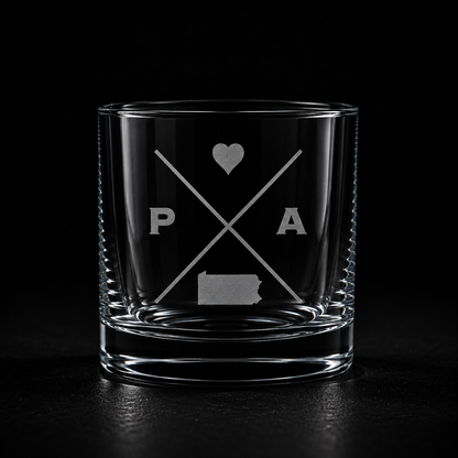 Engraved Pennsylvania rocks glass with frosted Pennsylvania silhouette and crossed-letter monogram on a dark background.