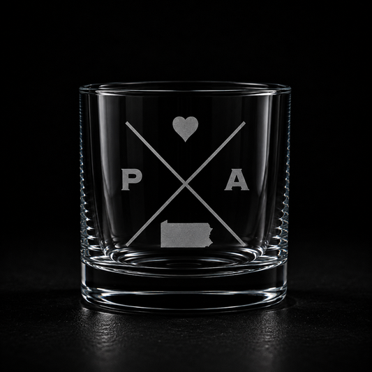 Engraved Pennsylvania rocks glass with frosted Pennsylvania silhouette and crossed-letter monogram on a dark background.