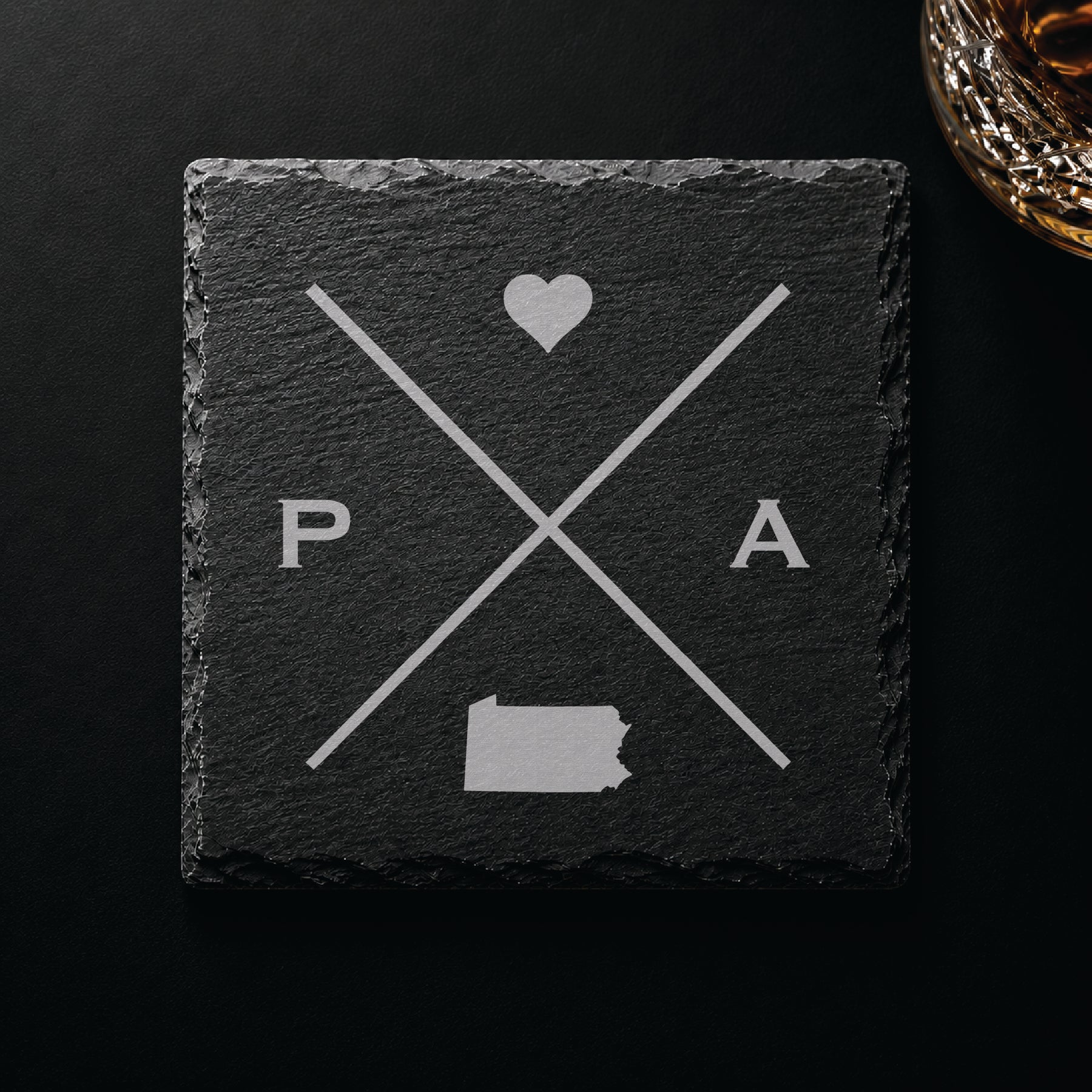 Dark slate coaster with engraved Pennsylvania crossed-line design, heart icon, and Pennsylvania silhouette on a dark background.