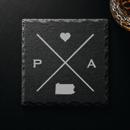 Dark slate coaster with engraved Pennsylvania crossed-line design, heart icon, and Pennsylvania silhouette on a dark background.
