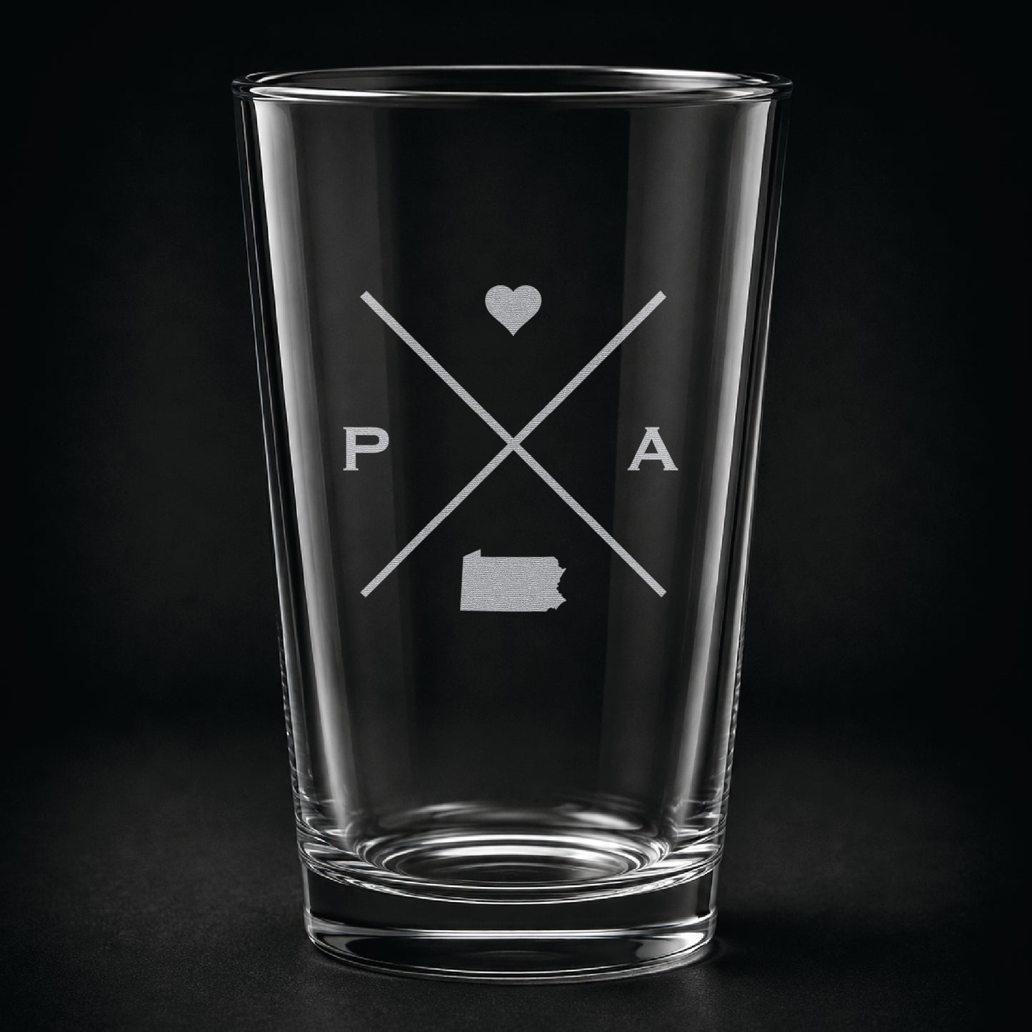 Engraved Pennsylvania pint glass featuring a minimalist crossed-line design with heart detail and Pennsylvania silhouette on a dark background.