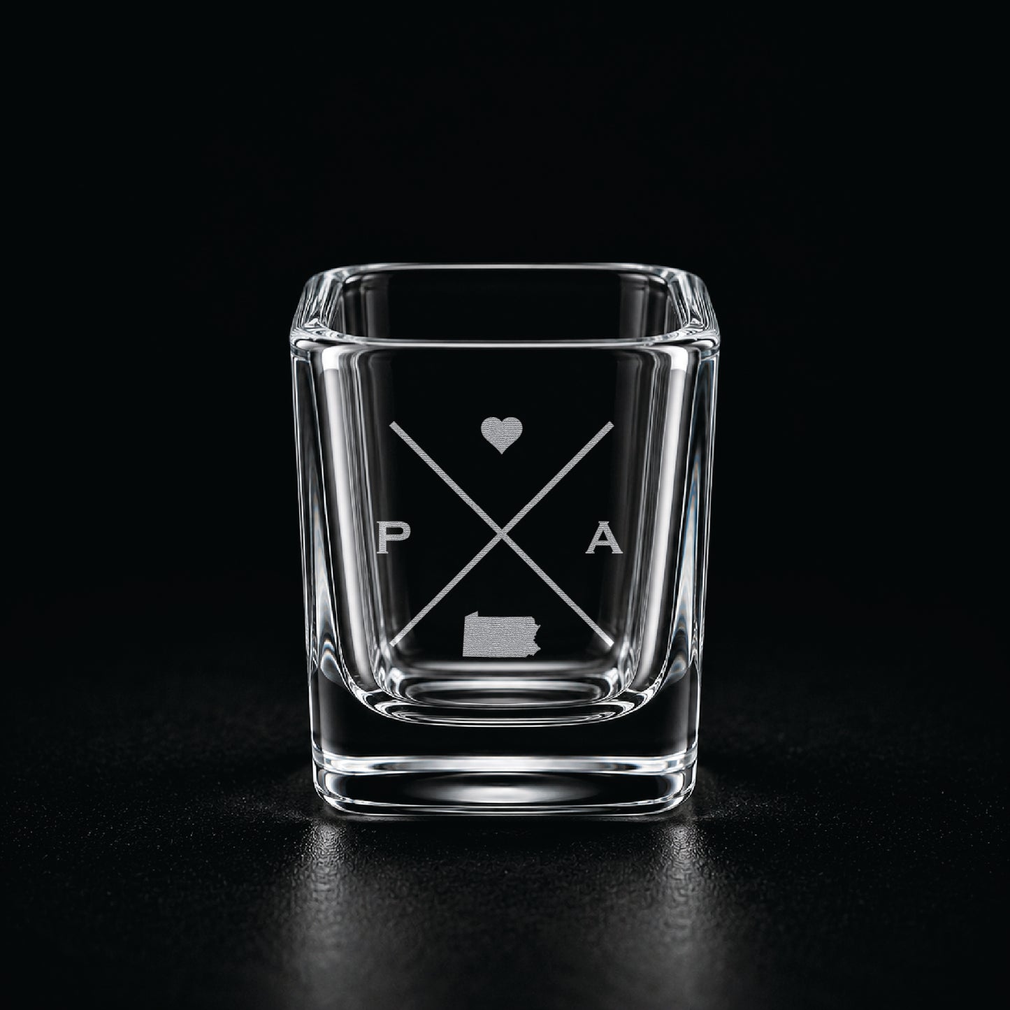 Engraved Pennsylvania shot glass with modern crossed-line state design and frosted laser engraving on a dark background.