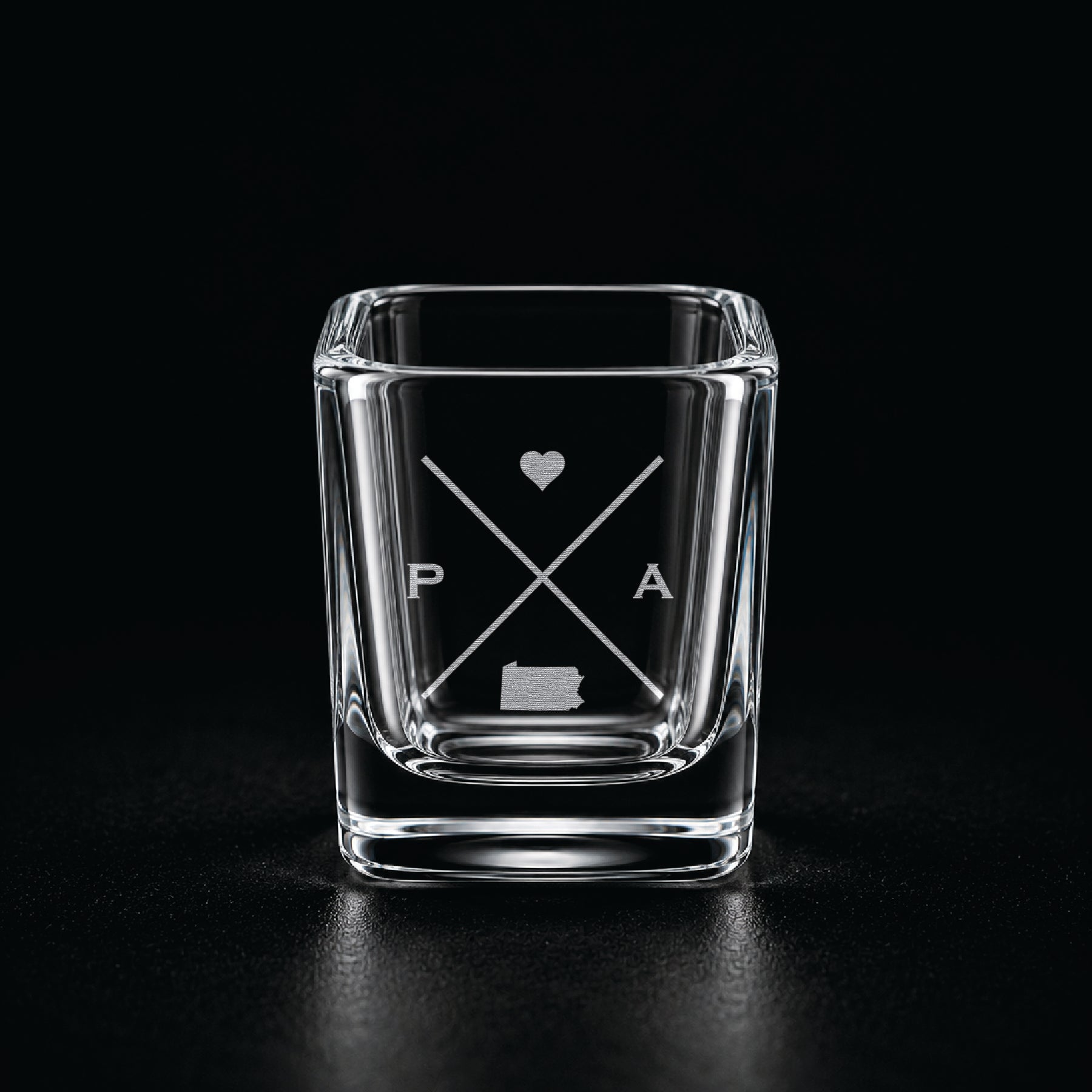 Engraved Pennsylvania shot glass with modern crossed-line state design and frosted laser engraving on a dark background.