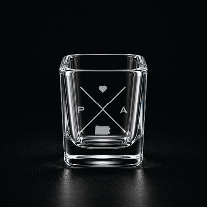 Engraved Pennsylvania shot glass with modern crossed-line state design and frosted laser engraving on a dark background.