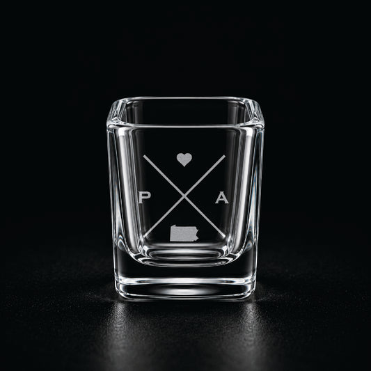 Engraved Pennsylvania shot glass with modern crossed-line state design and frosted laser engraving on a dark background.