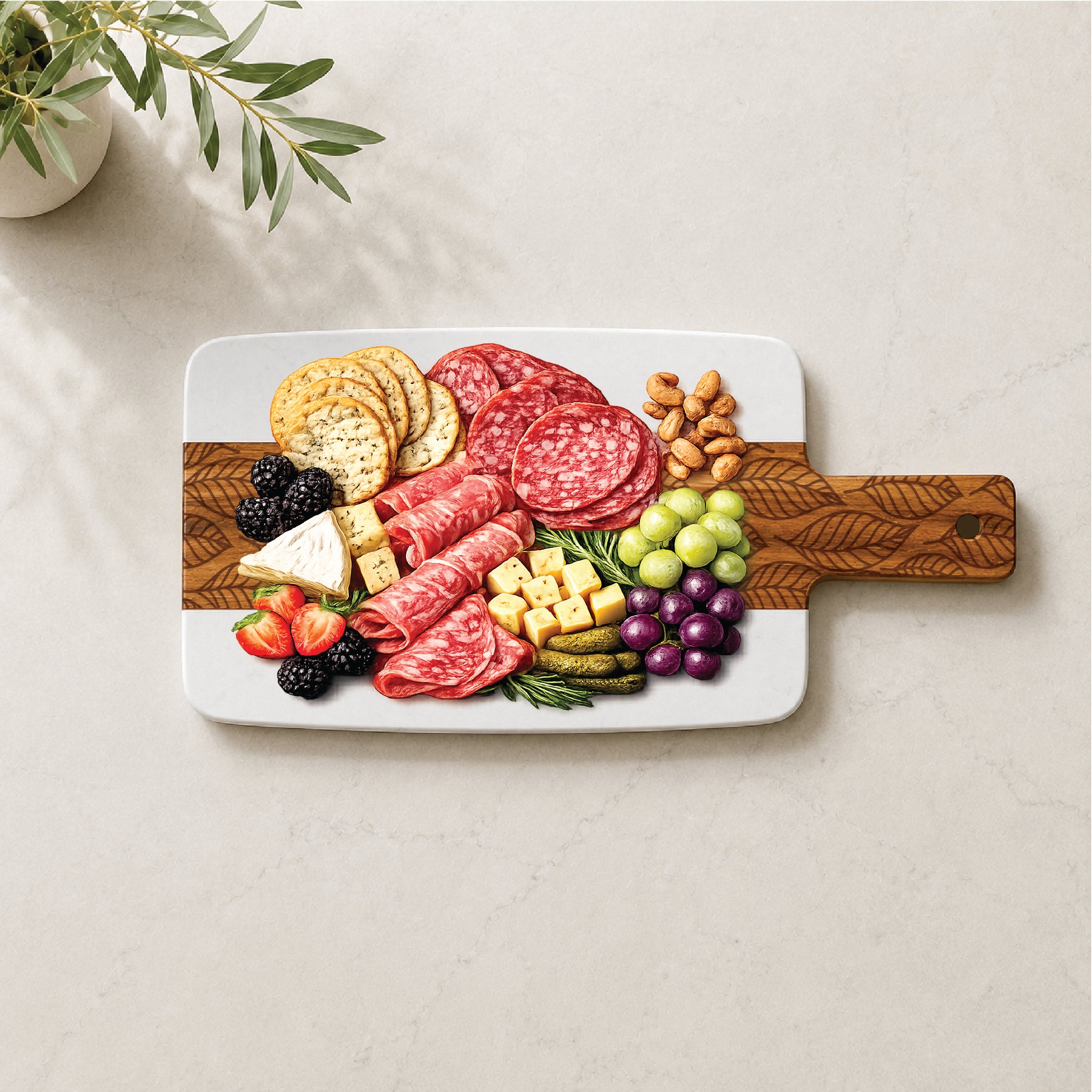 Marble and acacia charcuterie board with engraved falling leaf pattern, styled with cheese, crackers, salami, grapes, berries, almonds, and pickles.