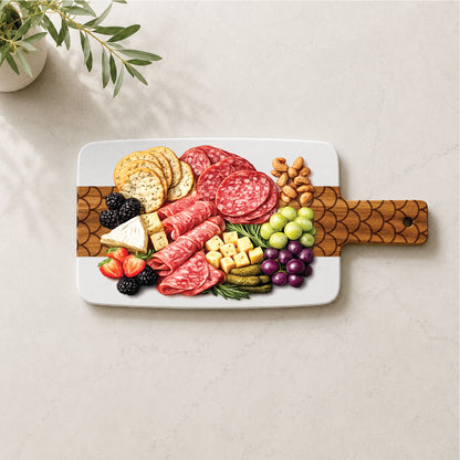 Marble and acacia charcuterie board with engraved scallop pattern styled with cheese, cured meats, fruit, crackers, and nuts.