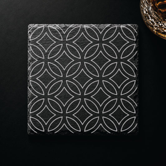 Geometric circle engraved slate coaster displayed beneath a whiskey glass on a dark tabletop.