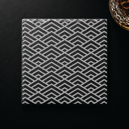Geometric Peaks engraved slate coaster displayed on a dark tabletop beside a whiskey glass, showcasing a modern geometric design.