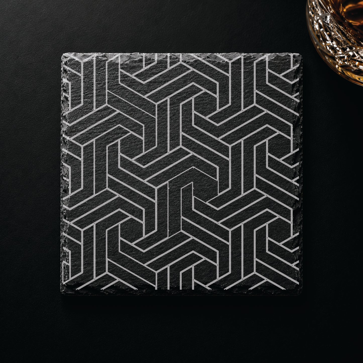 Modern Geometric engraved slate coaster displayed on a dark tabletop beside a whiskey glass, showcasing a contemporary geometric design.