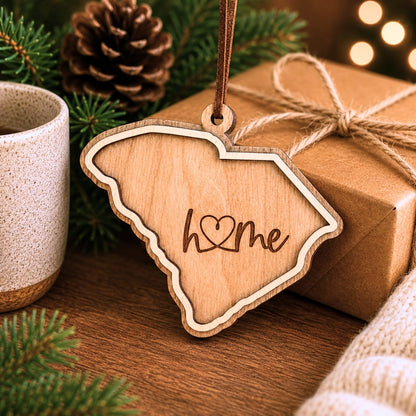 Layered South Carolina wood ornament with engraved “home” script displayed beside wrapped holiday gifts, greenery, and warm seasonal décor.