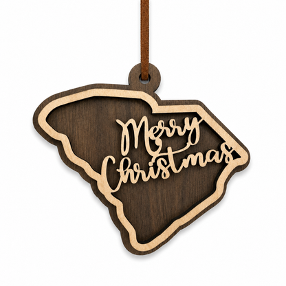 Layered South Carolina state Christmas ornament with walnut and maple wood and “Merry Christmas” script, photographed on a clean white background with faux leather hanger.