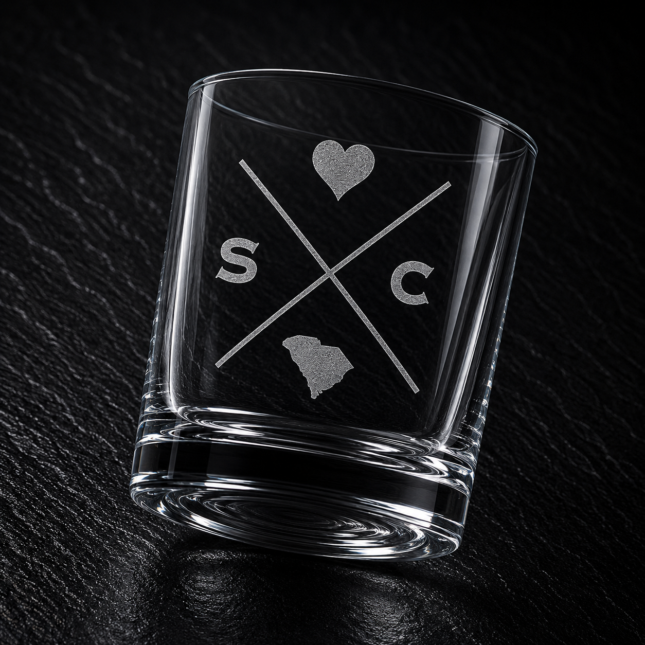 Angled engraved South Carolina whiskey glass featuring frosted South Carolina silhouette and modern crossed-letter design on a dark textured surface.