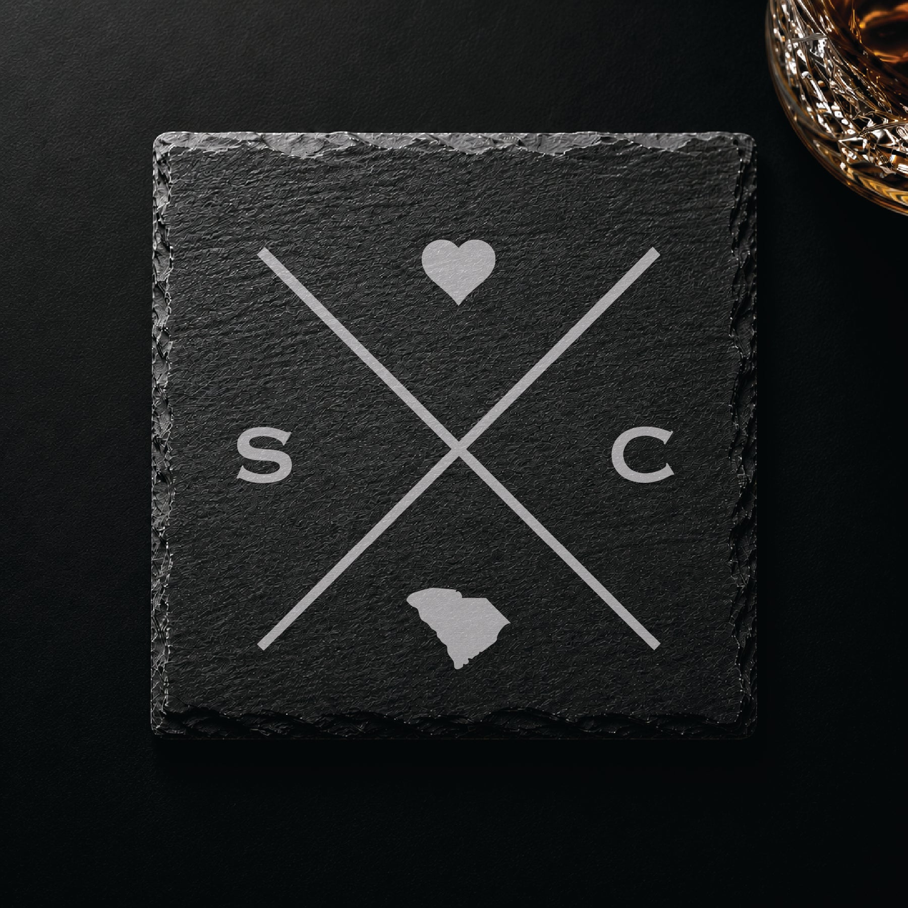 Dark slate coaster with engraved South Carolina crossed-line design, heart icon, and South Carolina silhouette on a dark background.