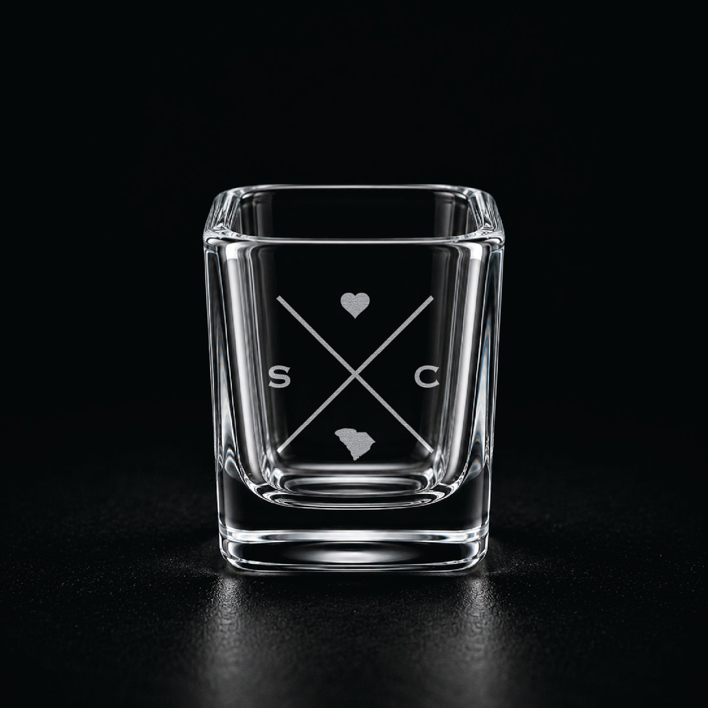 Engraved South Carolina shot glass with modern crossed-line state design and frosted laser engraving on a dark background.