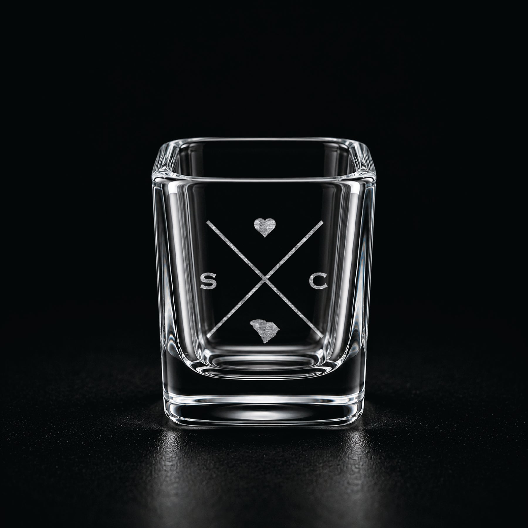 Engraved South Carolina shot glass with modern crossed-line state design and frosted laser engraving on a dark background.