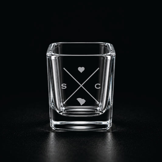Engraved South Carolina shot glass with modern crossed-line state design and frosted laser engraving on a dark background.