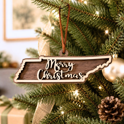 Layered Tennessee state Christmas ornament hanging on a decorated holiday tree, featuring walnut and maple wood tones, “Merry Christmas” script, warm white lights, and neutral festive décor.