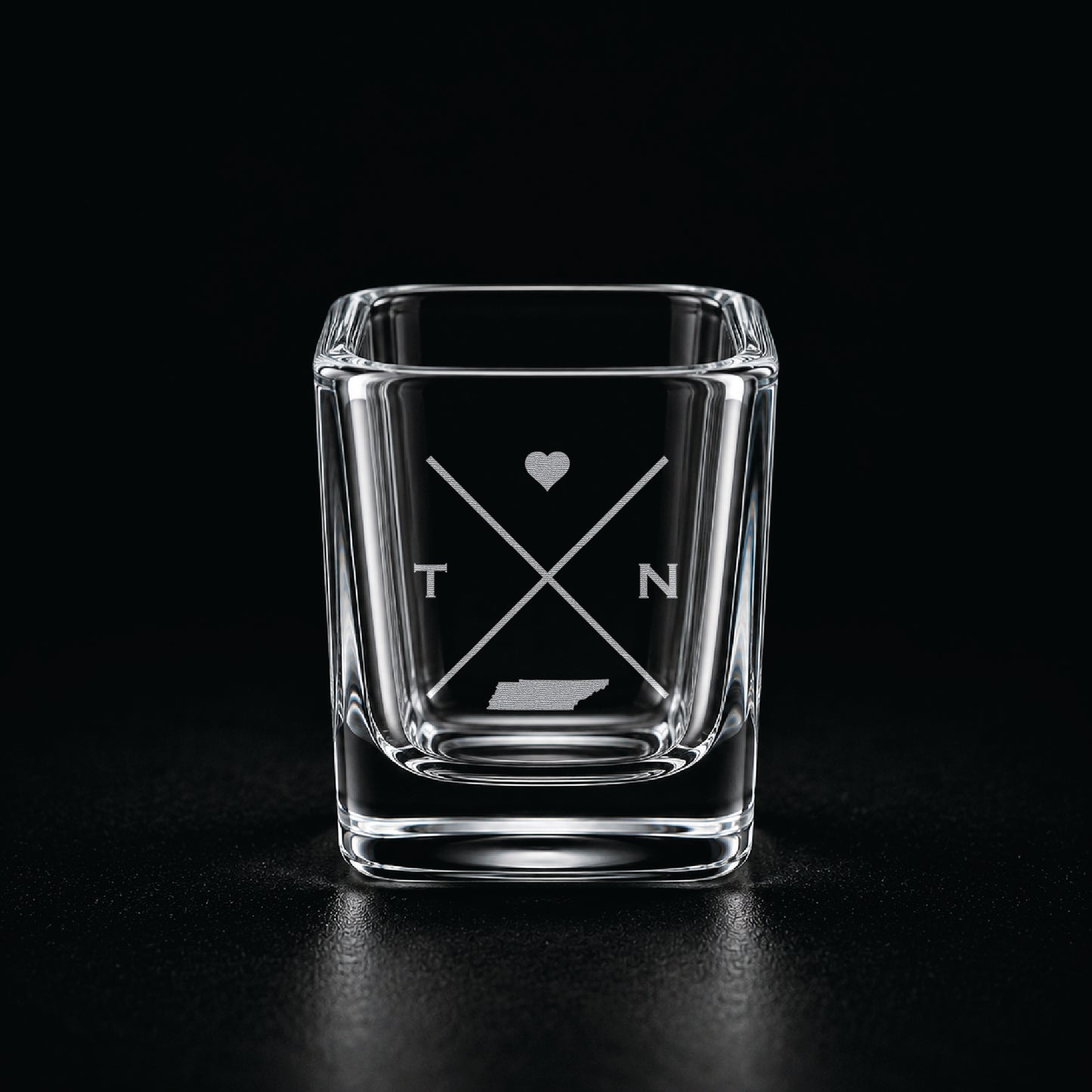 Engraved Tennessee shot glass with modern crossed-line state design and frosted laser engraving on a dark background.