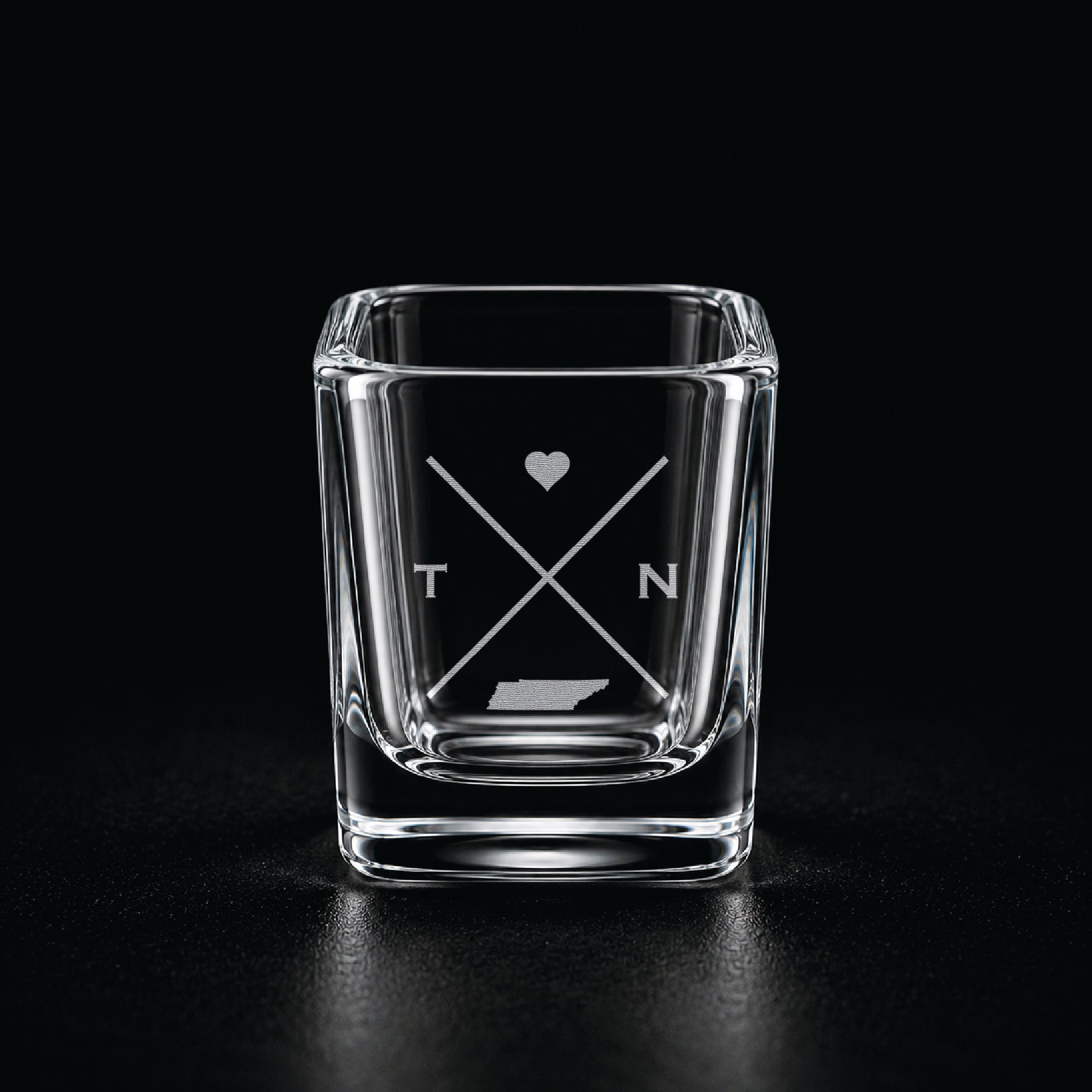 Engraved Tennessee shot glass with modern crossed-line state design and frosted laser engraving on a dark background.
